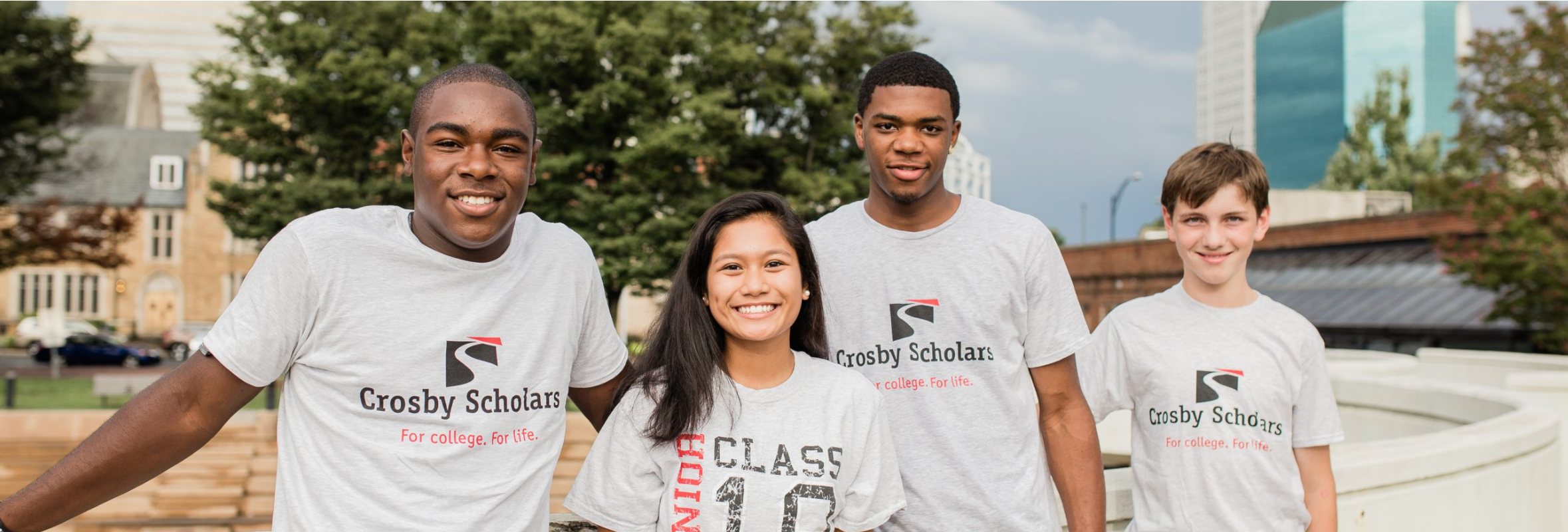 A group of 4 children and teens, smiling and wearing Crosby Scholars shirts.