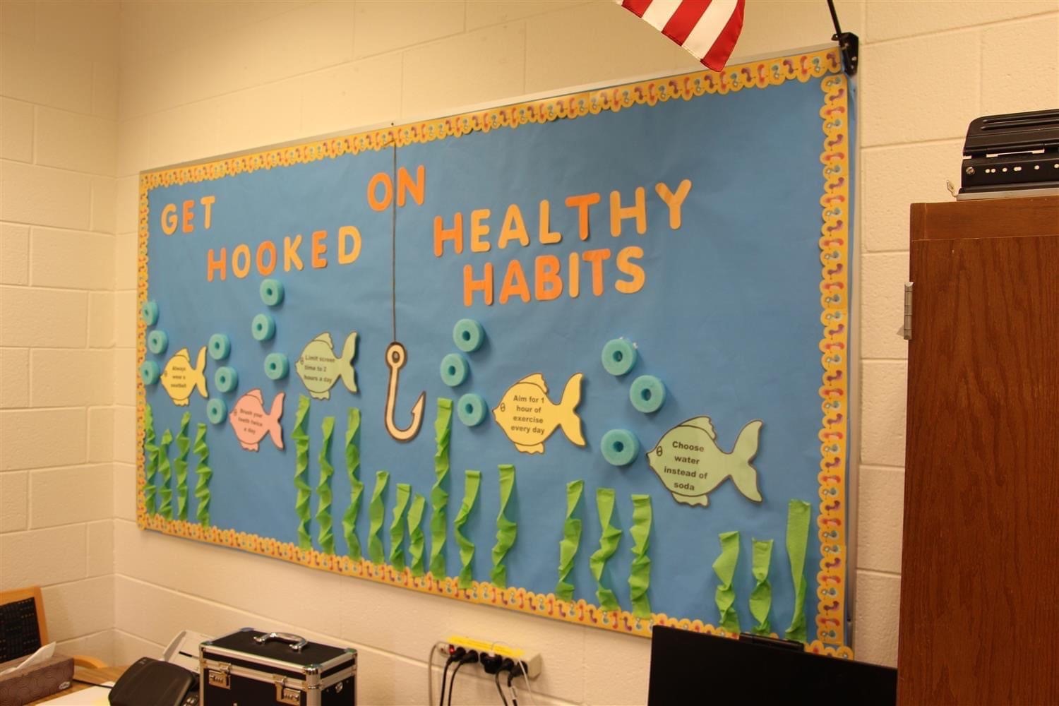 Cutout paper letters on a fish themed bulletin board. Text reads: Get Hooked on Healthy Habits