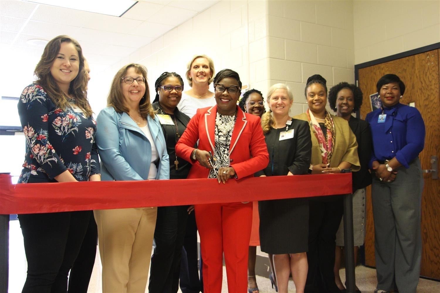 School Health Alliance members standing behind a ribbon at the ribbon cutting ceremony at Petree Elementary School. It is 10 people in business attire.